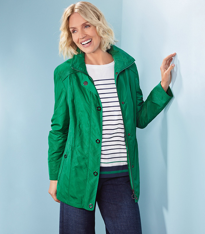 A woman smiling in an emerald green seasonal coat and a navy, white and green cotton striped jumper. 